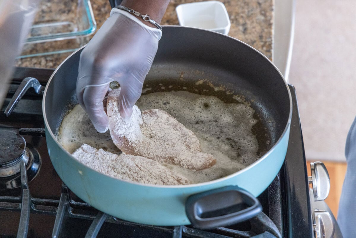 adding floured chicken breast to skillet