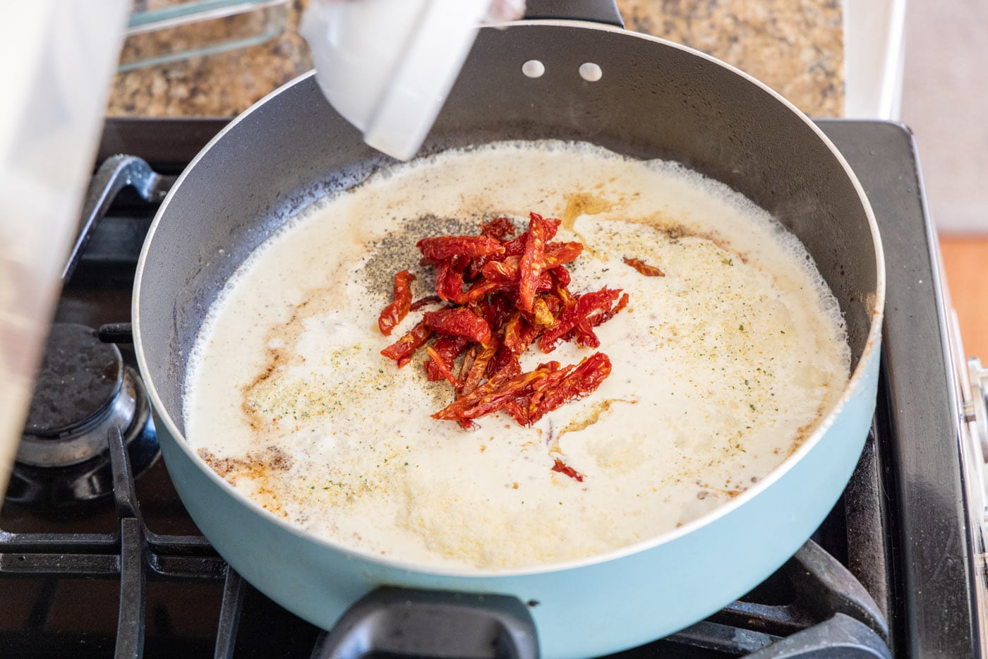 adding sun dried tomatoes to heavy cream mixture in skillet