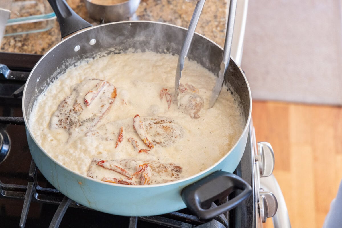flipping chicken breasts in a skillet with heavy cream sauce
