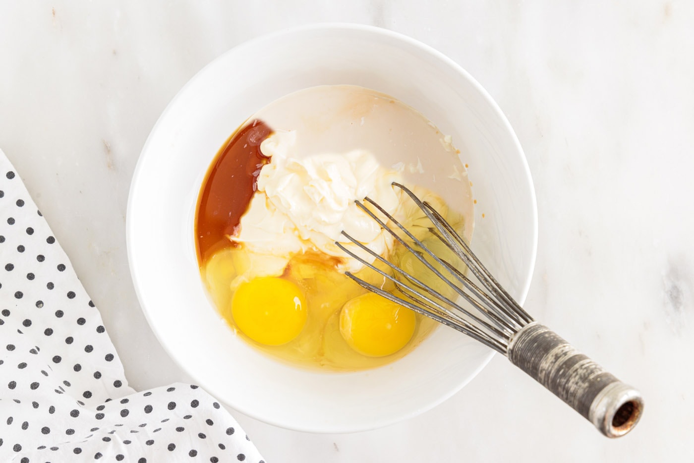 whisking eggs, milk, mayonnaise, and vanilla in abowl