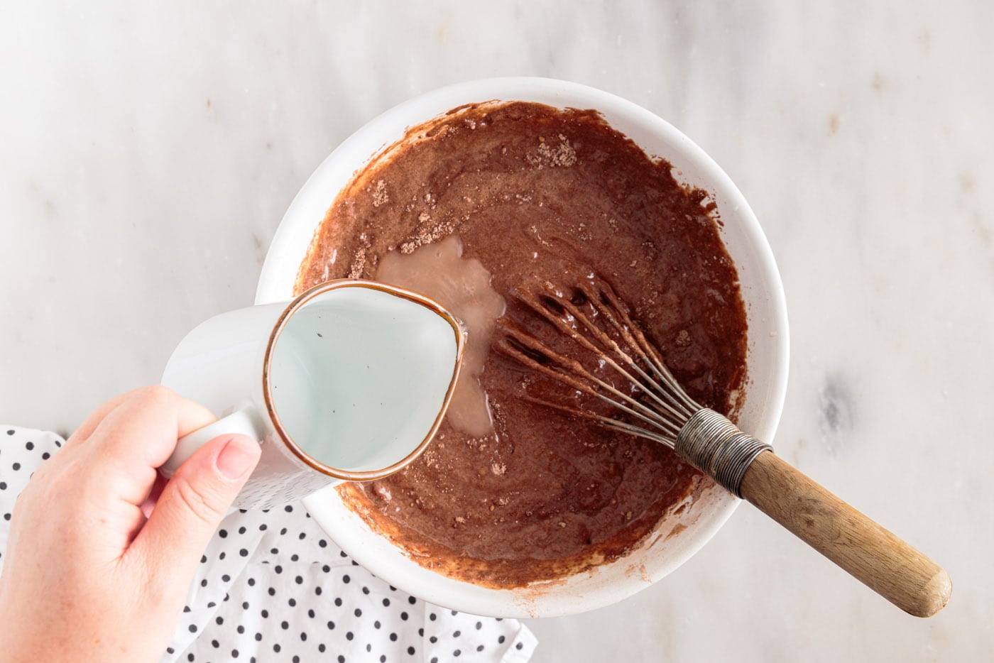 adding hot water to chocolate cake batter in a bowl