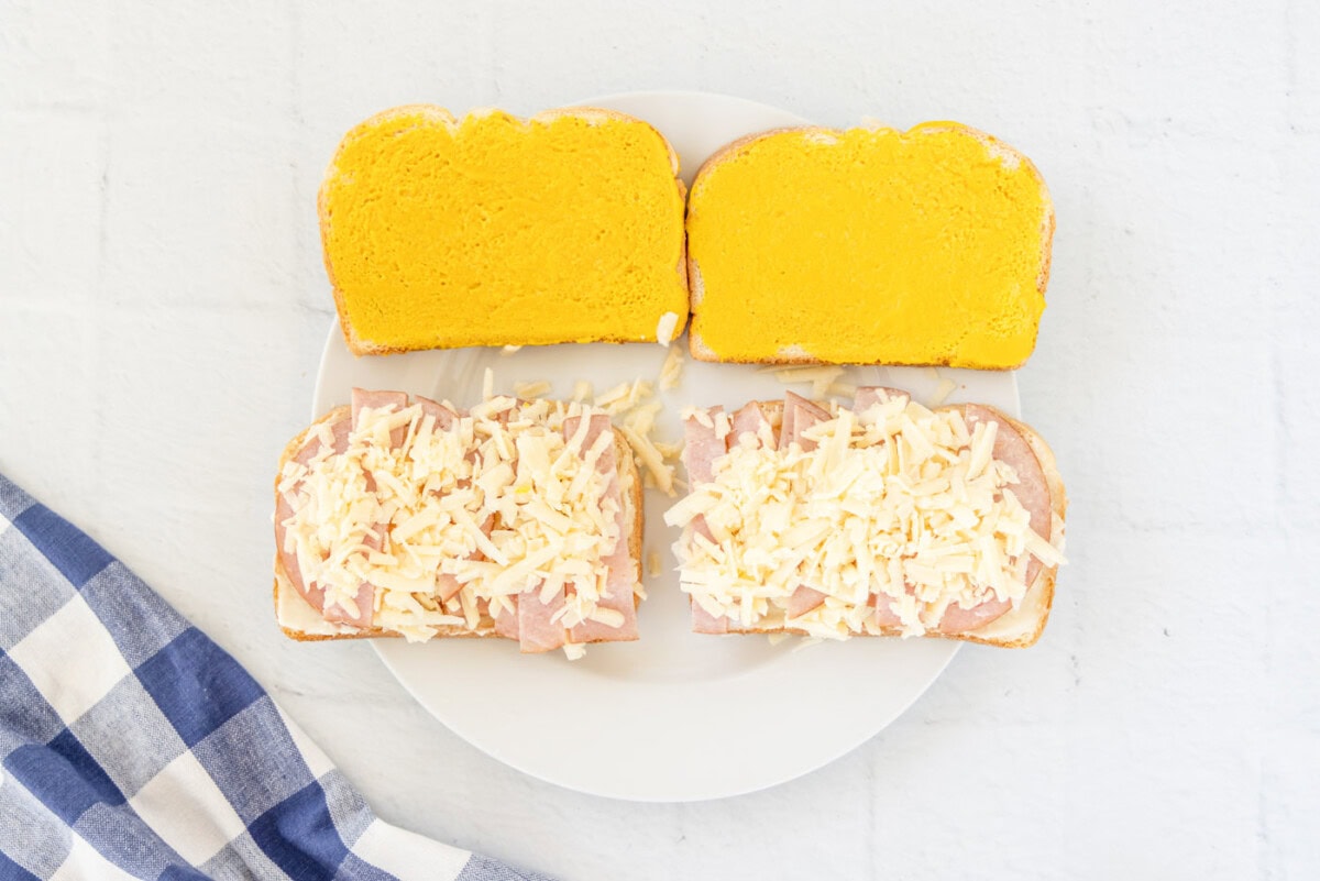 shredded gruyere cheese on top of mayo and ham on bread