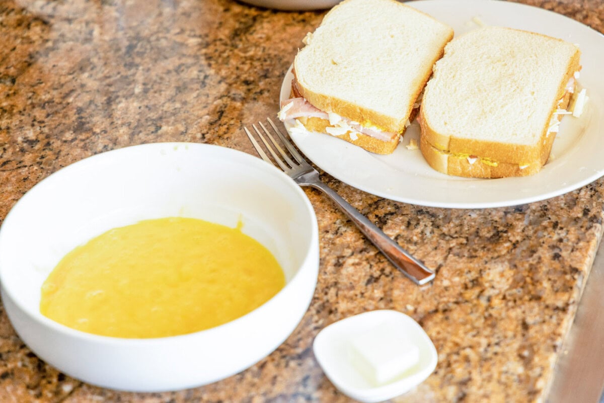 whisked eggs in a bowl and monte cristo sandwich on the side