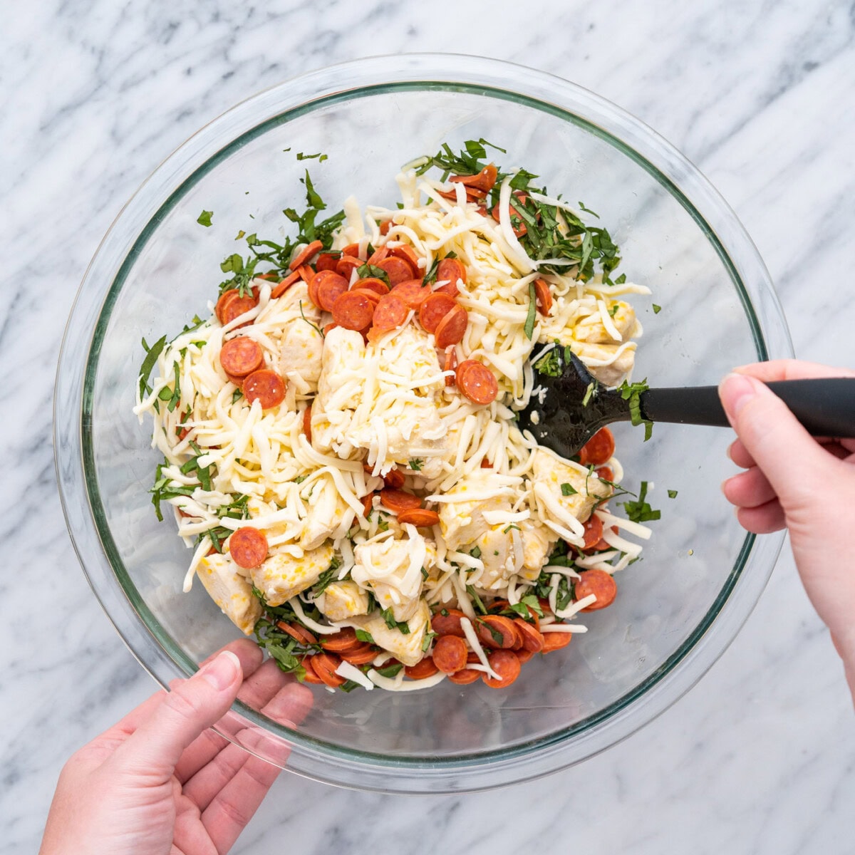 mixing mini pepperonis, biscuit dough, basil, and mozzarella cheese in a bowl