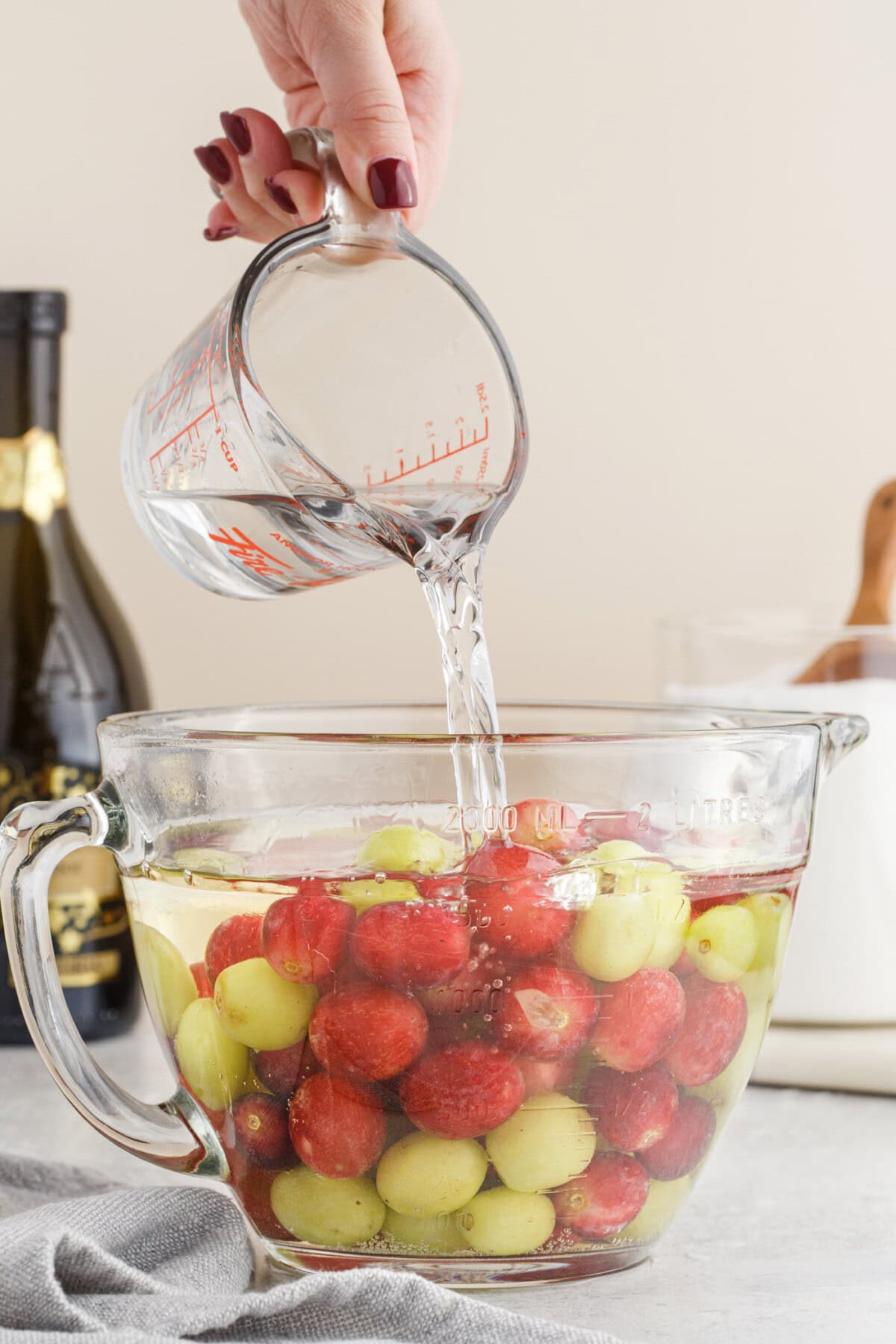 pouring vodka over prosecco and grapes in a bowl