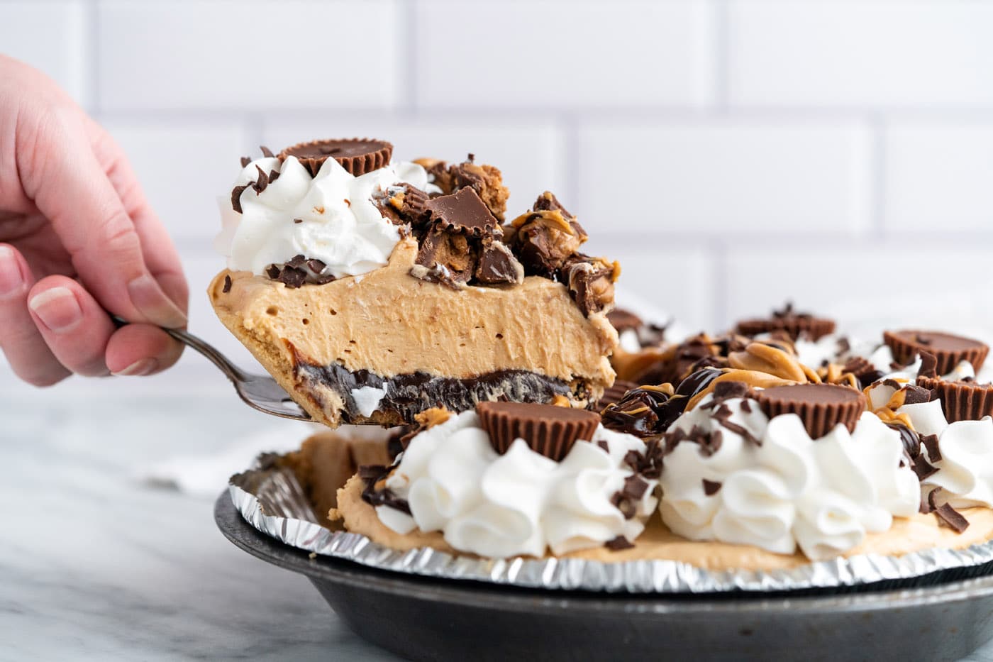 This Reeses pie is piled high with whipped cream, Reese's peanut butter cups, shaved chocolate, melt