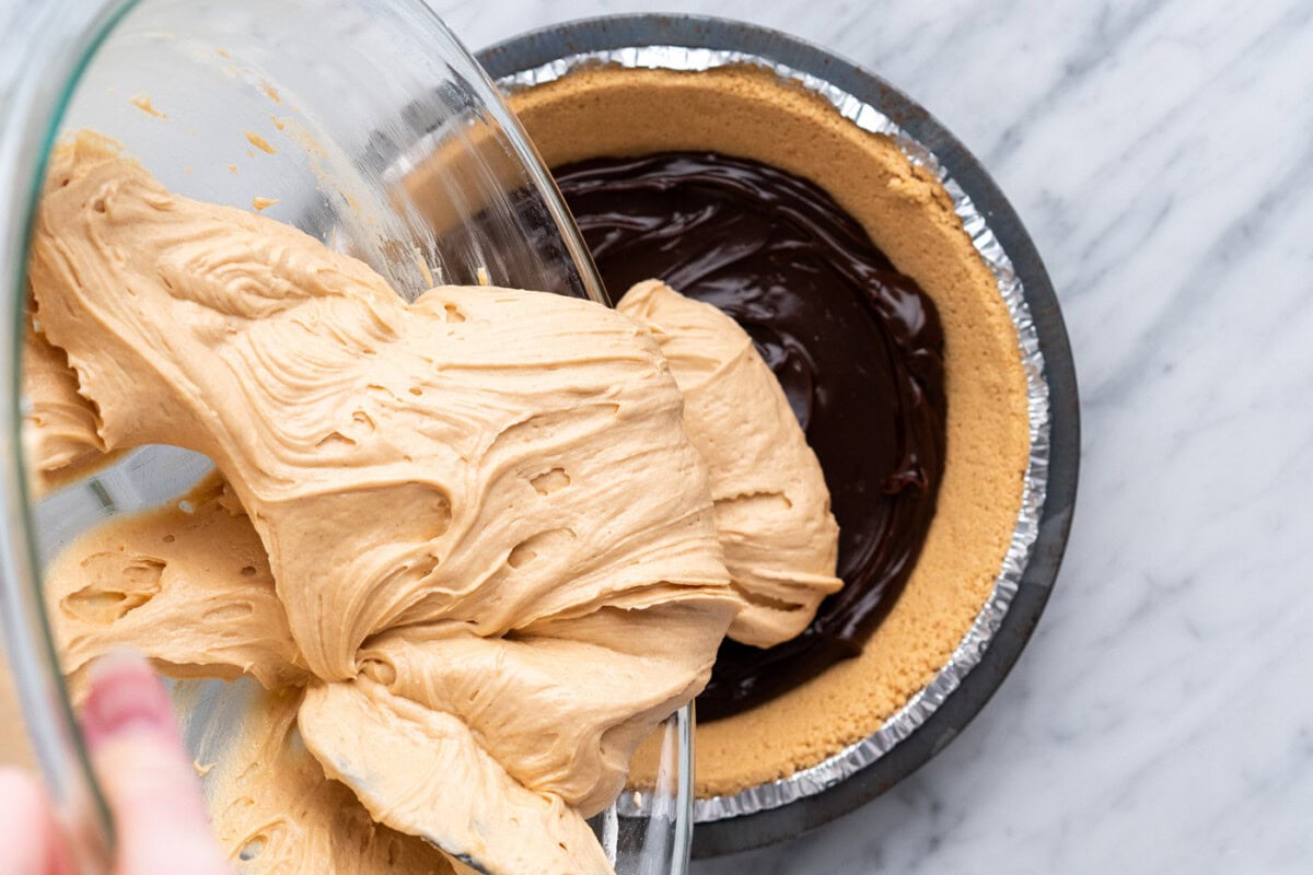 pouring creamy peanut butter mixture over hot fudge pie