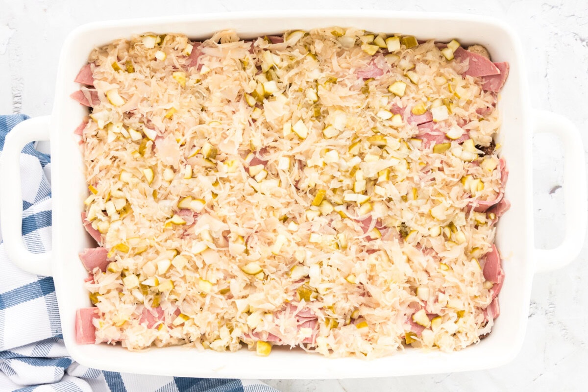 sauerkraut and pickles on top of sliced corned beef in a baking dish