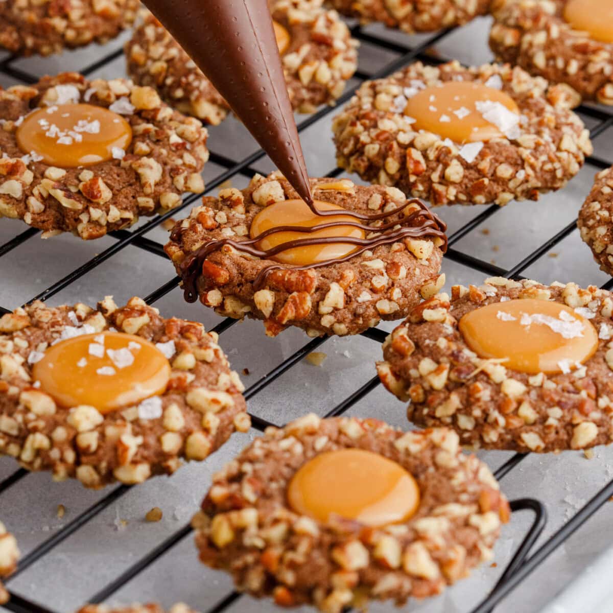 drizzling chocolate over turtle thumbprint cookies