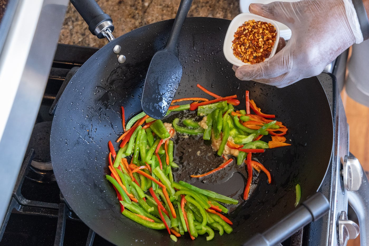 adding red pepper flakes to veggies in a wok