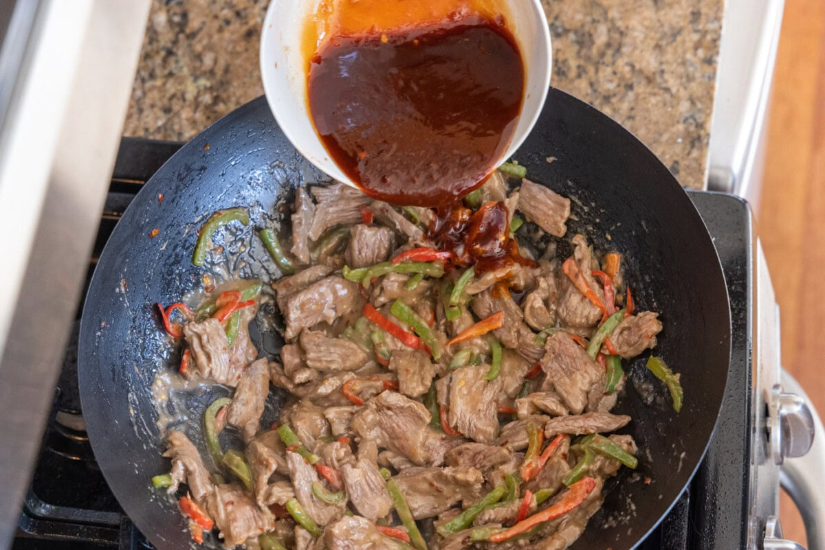 pouring sauce into kung pao beef in a wok