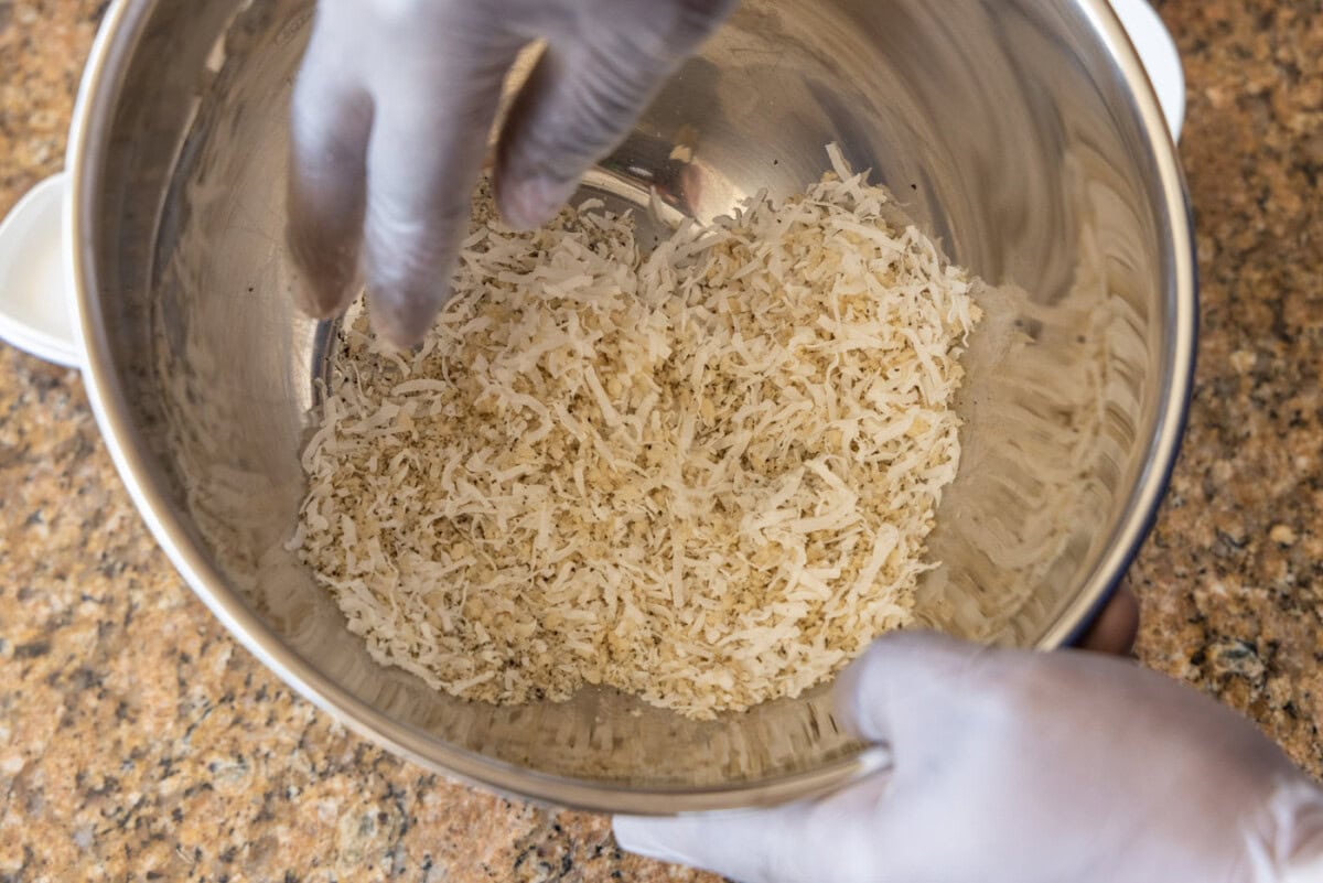 hands tossing coconut with breadcrumbs in a bowl