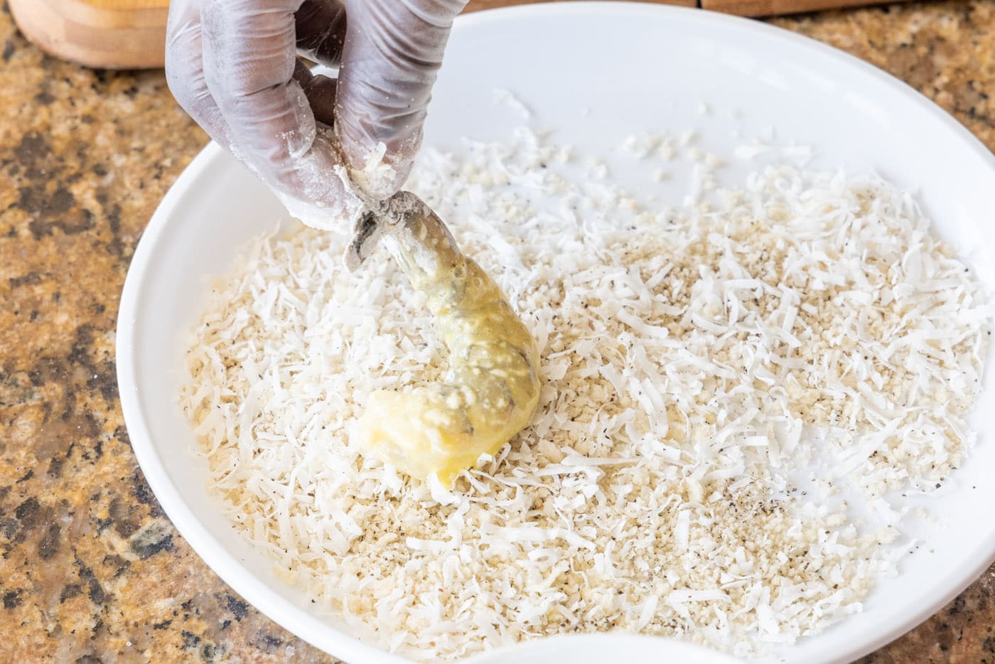 pressing flour and egg coated shrimp into coconut and breadcrumbs