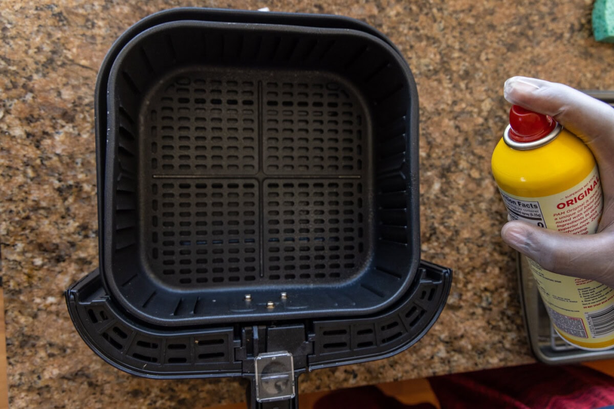 spraying air fryer with cooking spray