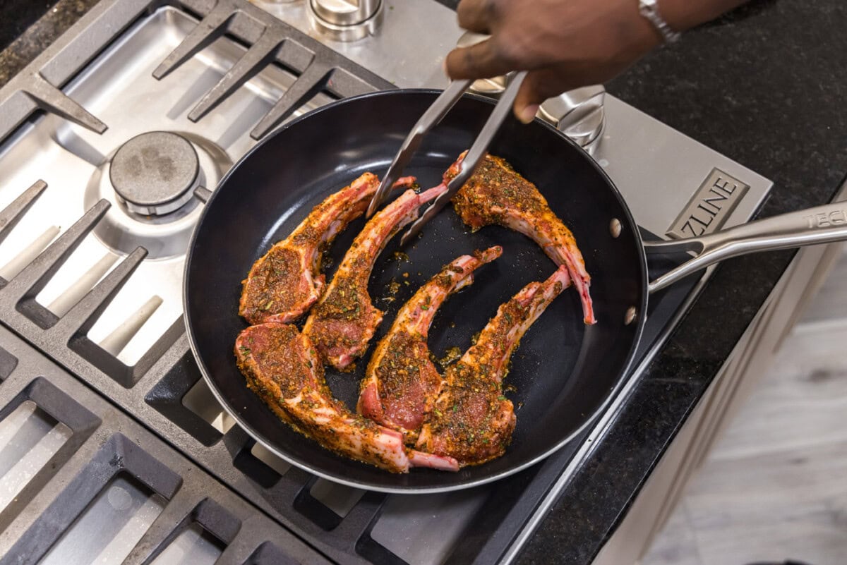 tongs moving lamb chop in a skillet