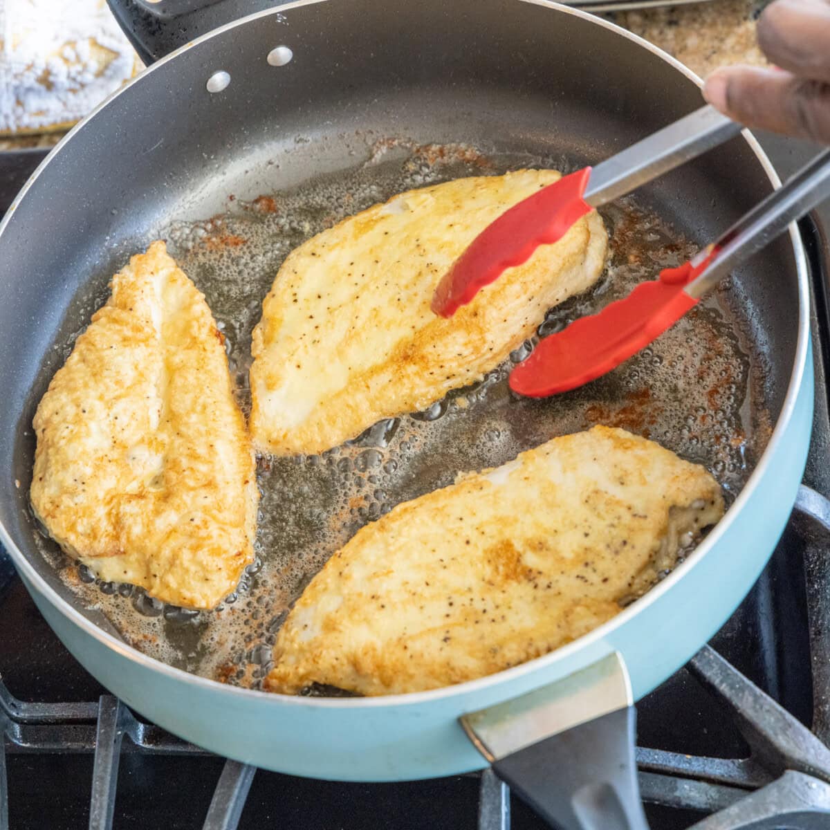 chicken breasts in a skillet with tongs