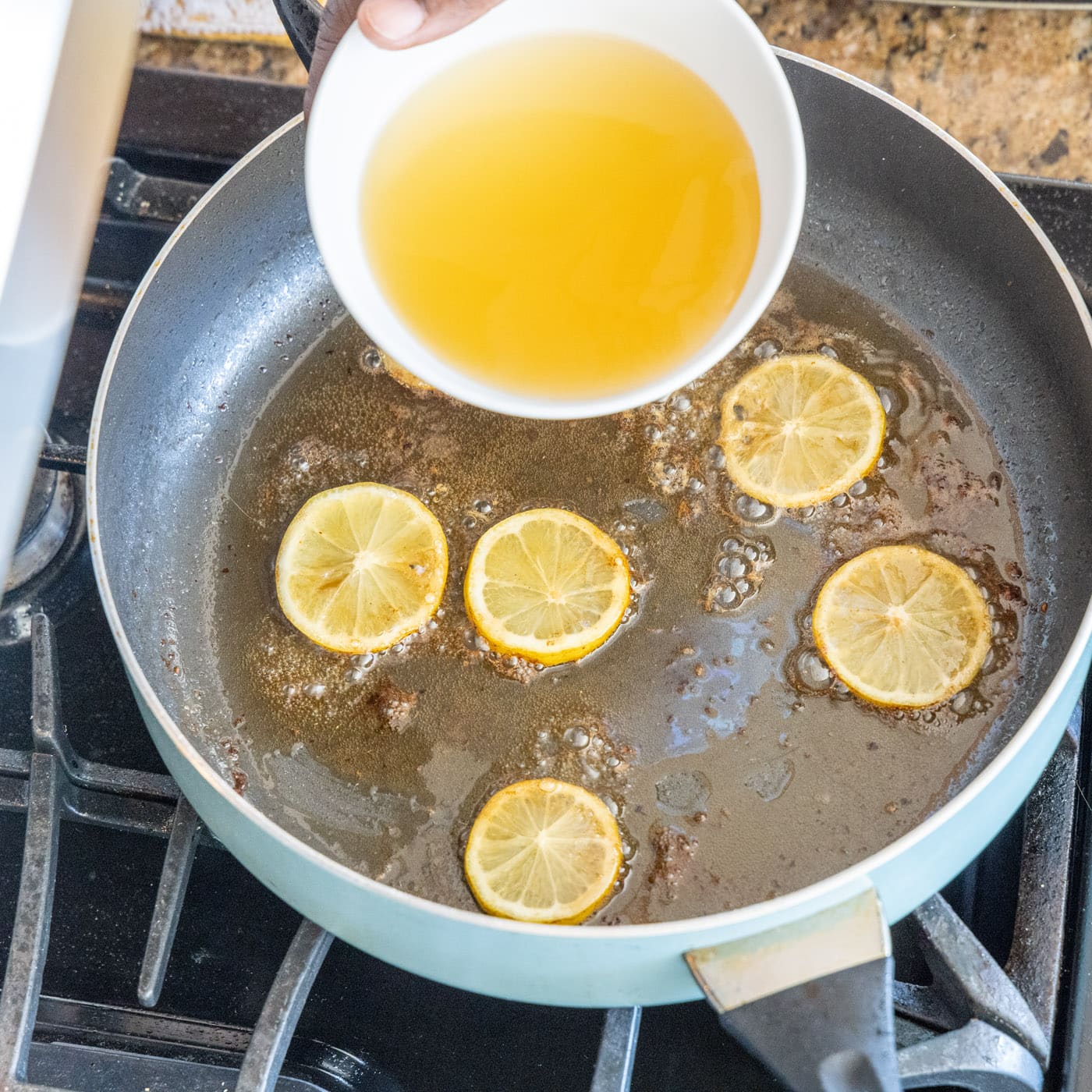 adding chicken stock to lemon and chicken pan juices