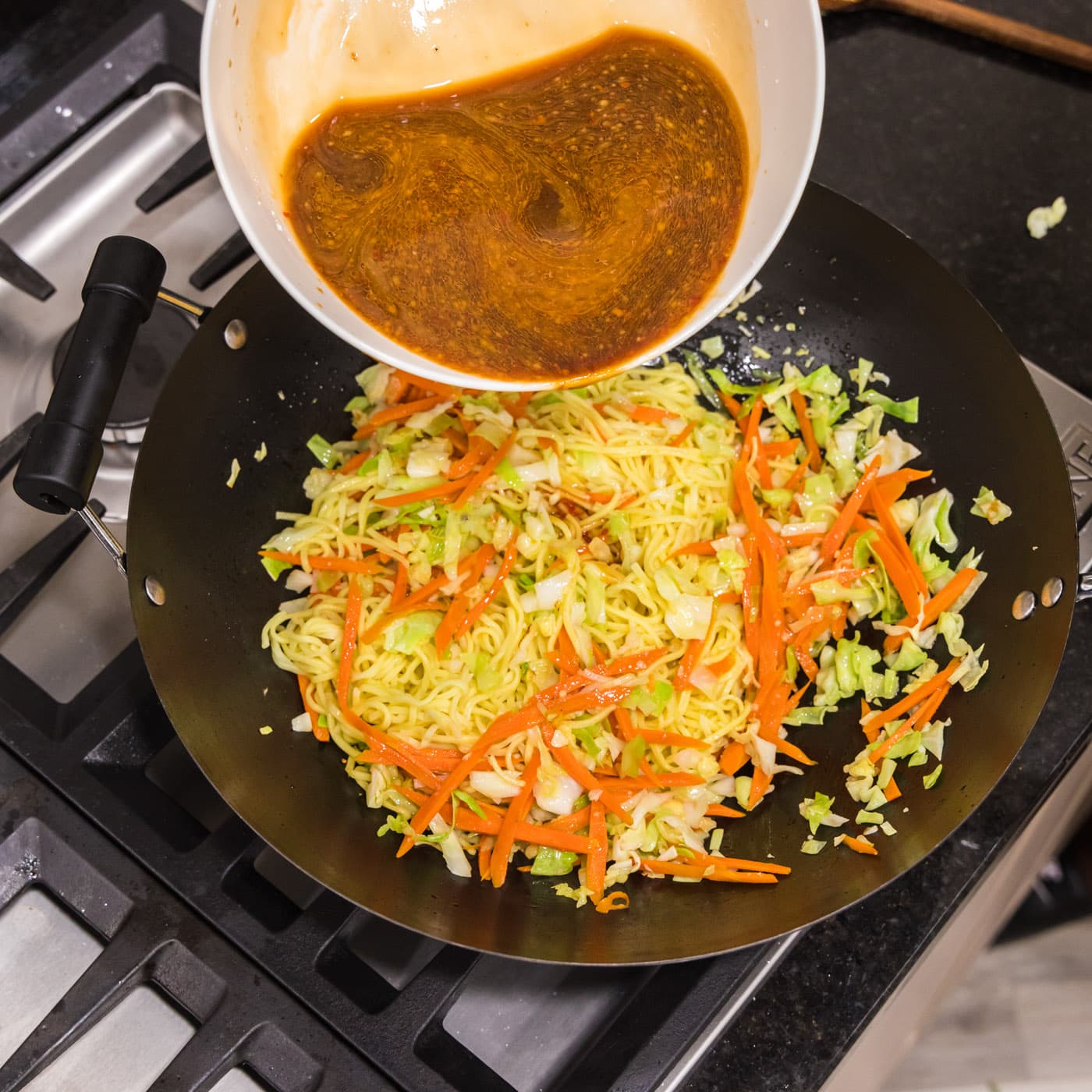 pouring chow mein sauce into wok with vegetables