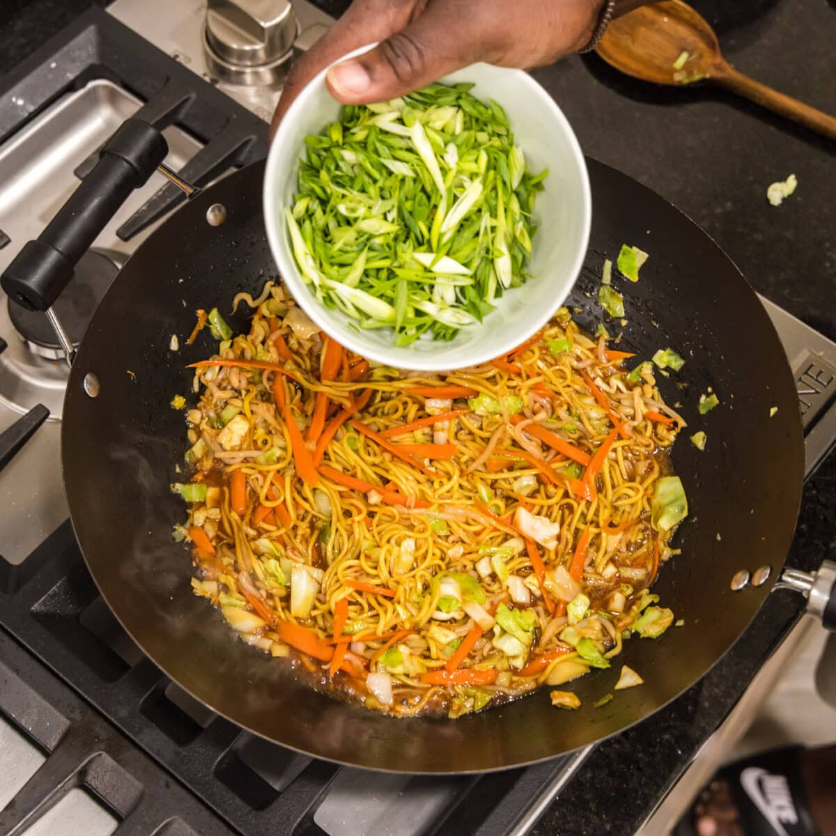 adding green onions to skillet of chow mein