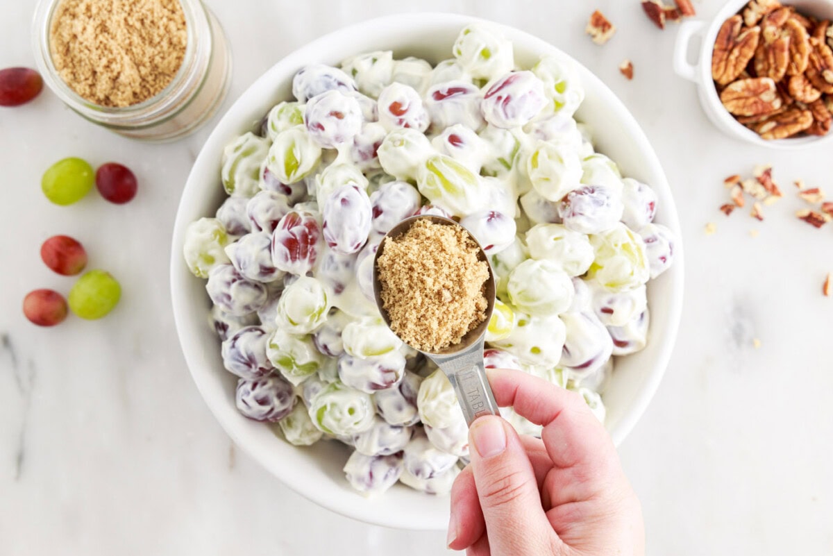 holding brown sugar over bowl of grape salad