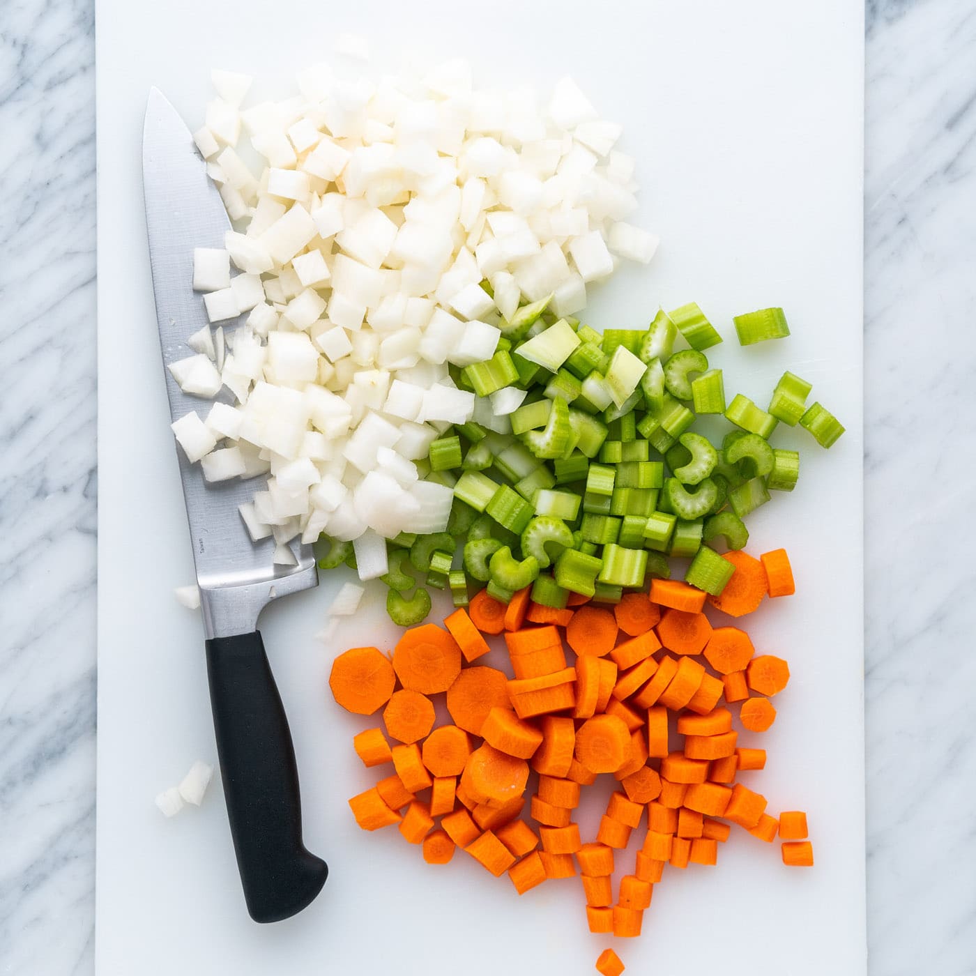 diced celery, onion, and carrots on a cutting board