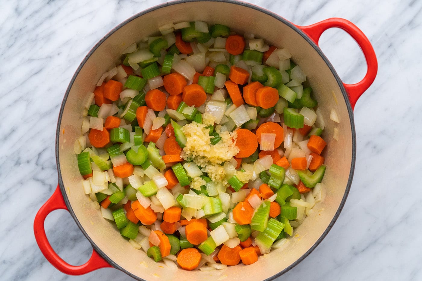 adding minced garlic to onion, celery, and carrots in a pot