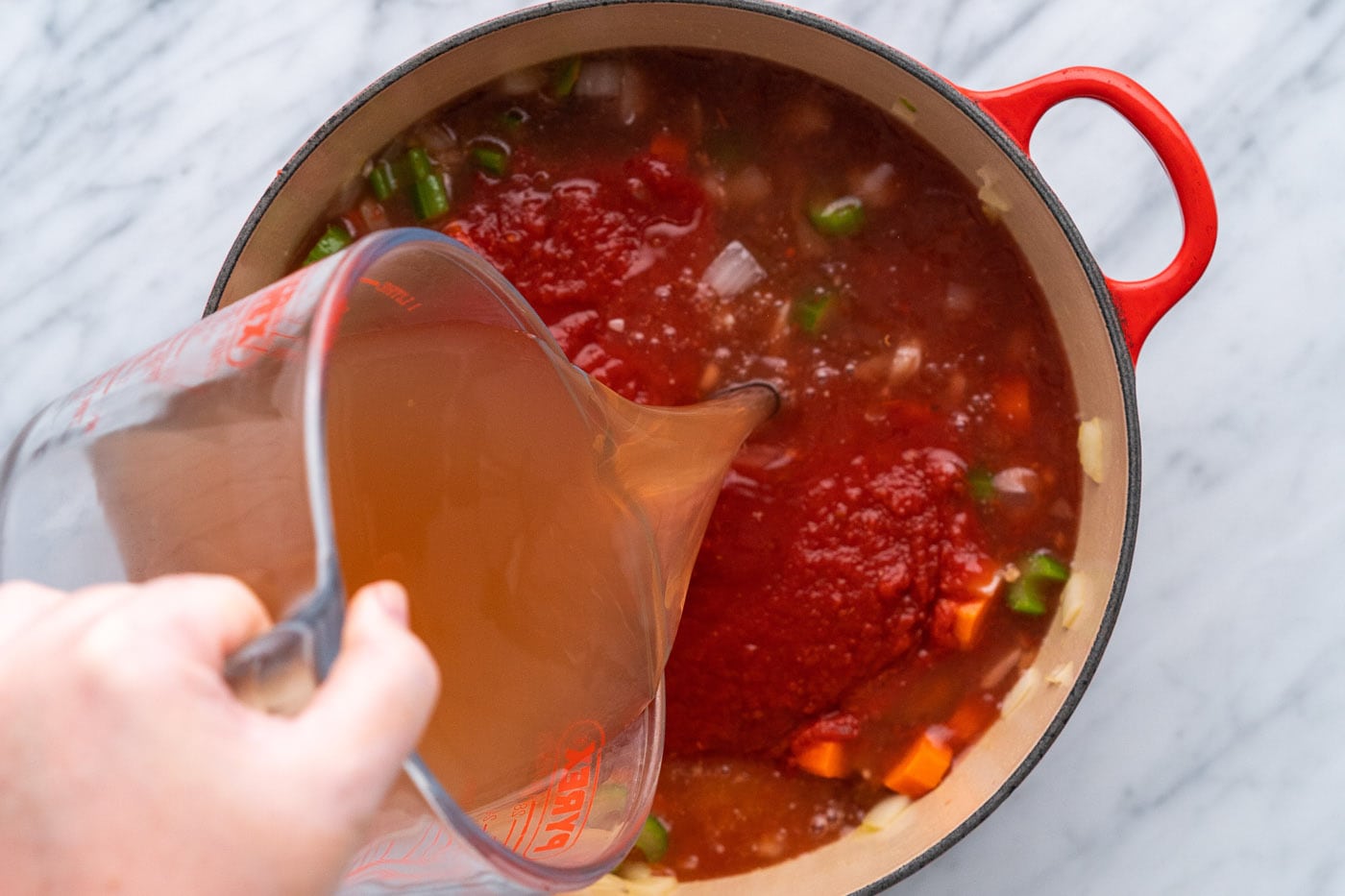 pouring vegetable broth over diced tomatoes, celery, onion, and carrot