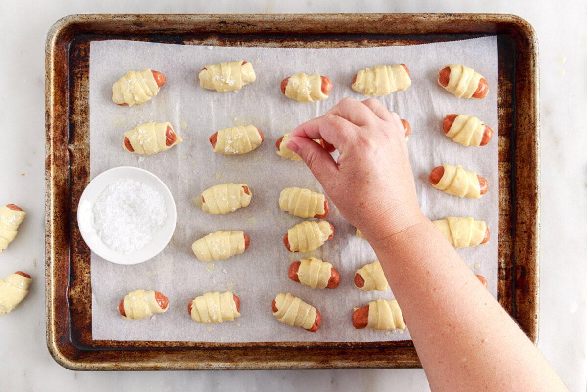 hand sprinkling salt over pigs in a blanket