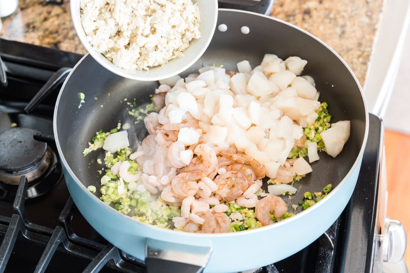 adding seafood to skillet with garlic and green onions
