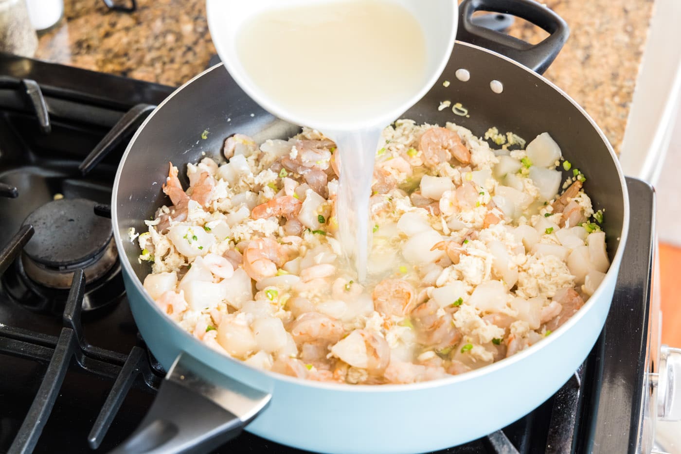 pouring stock into seafood lasagna ingredients