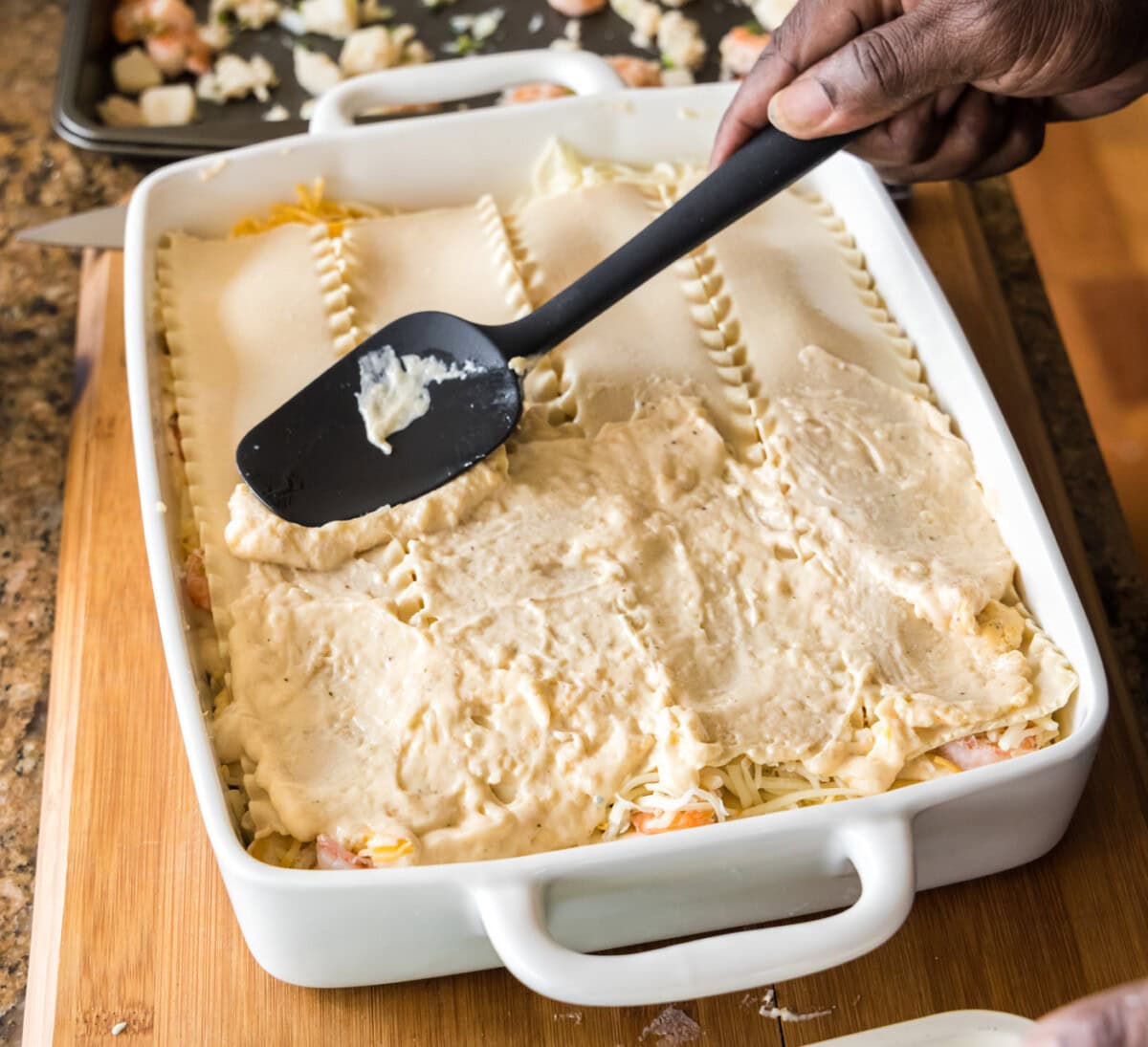 spreading cream sauce over lasagna noodles