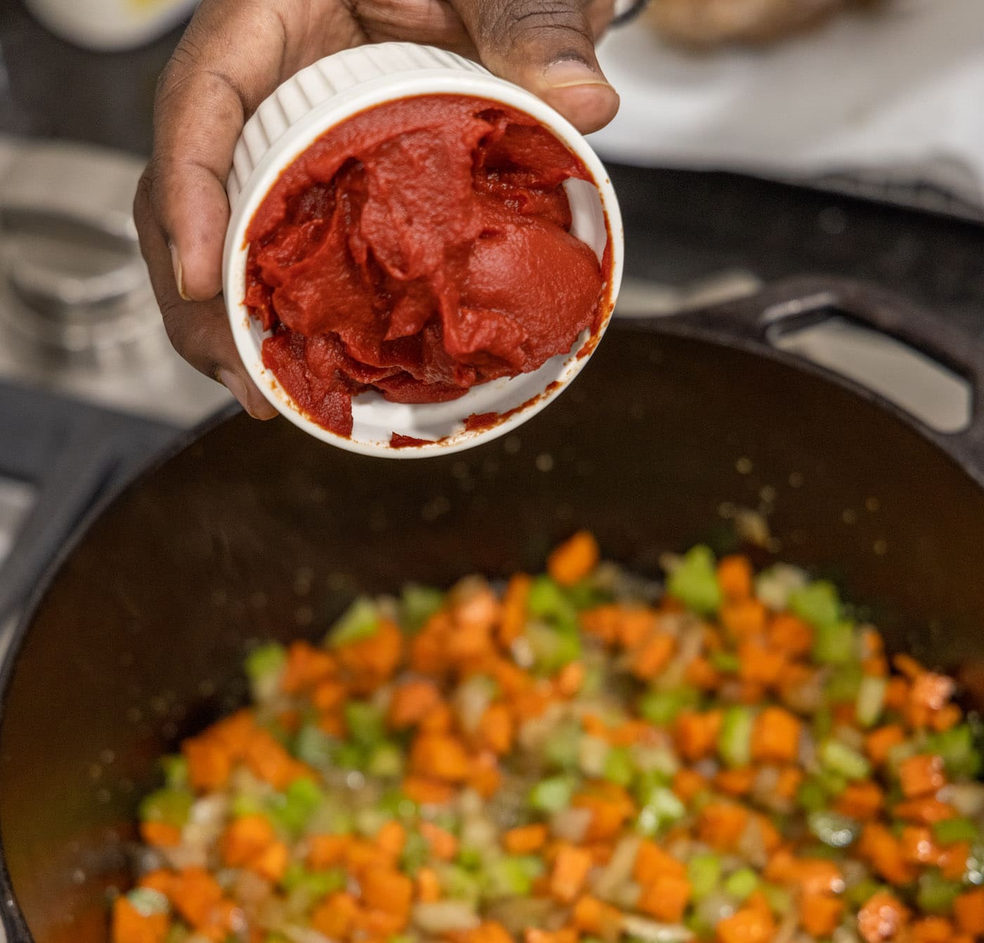 adding tomato paste to celery, onion, and carrots in a dutch oven