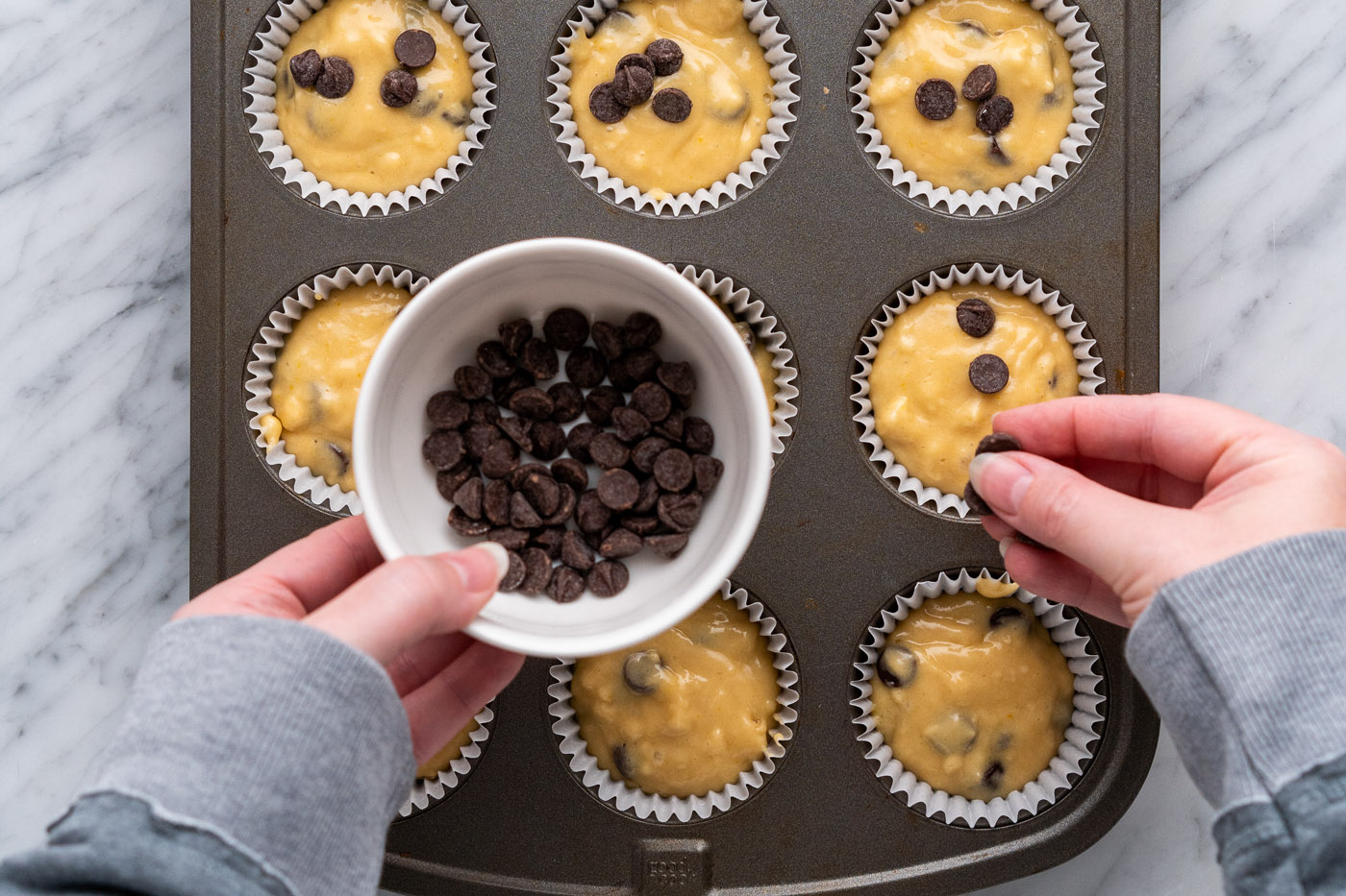 adding extra chocolate chips on top of muffin batter in a pan