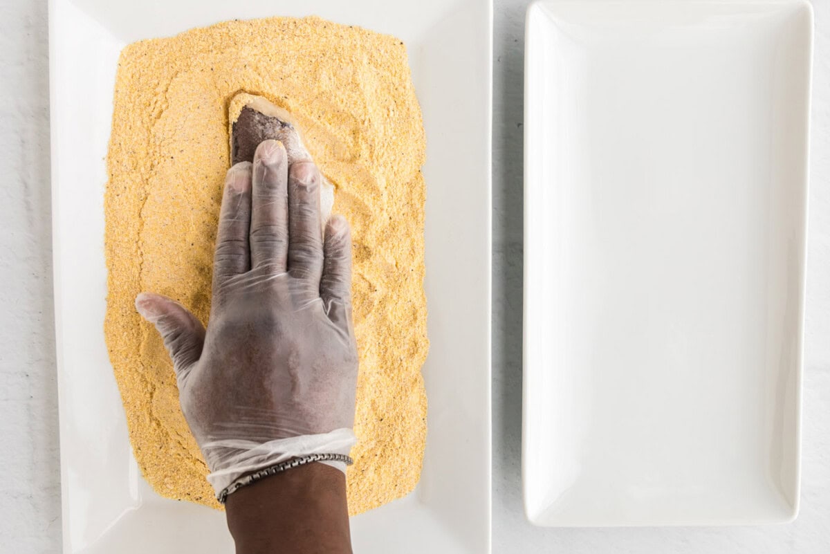 pressing fish filet into cornmeal mixture