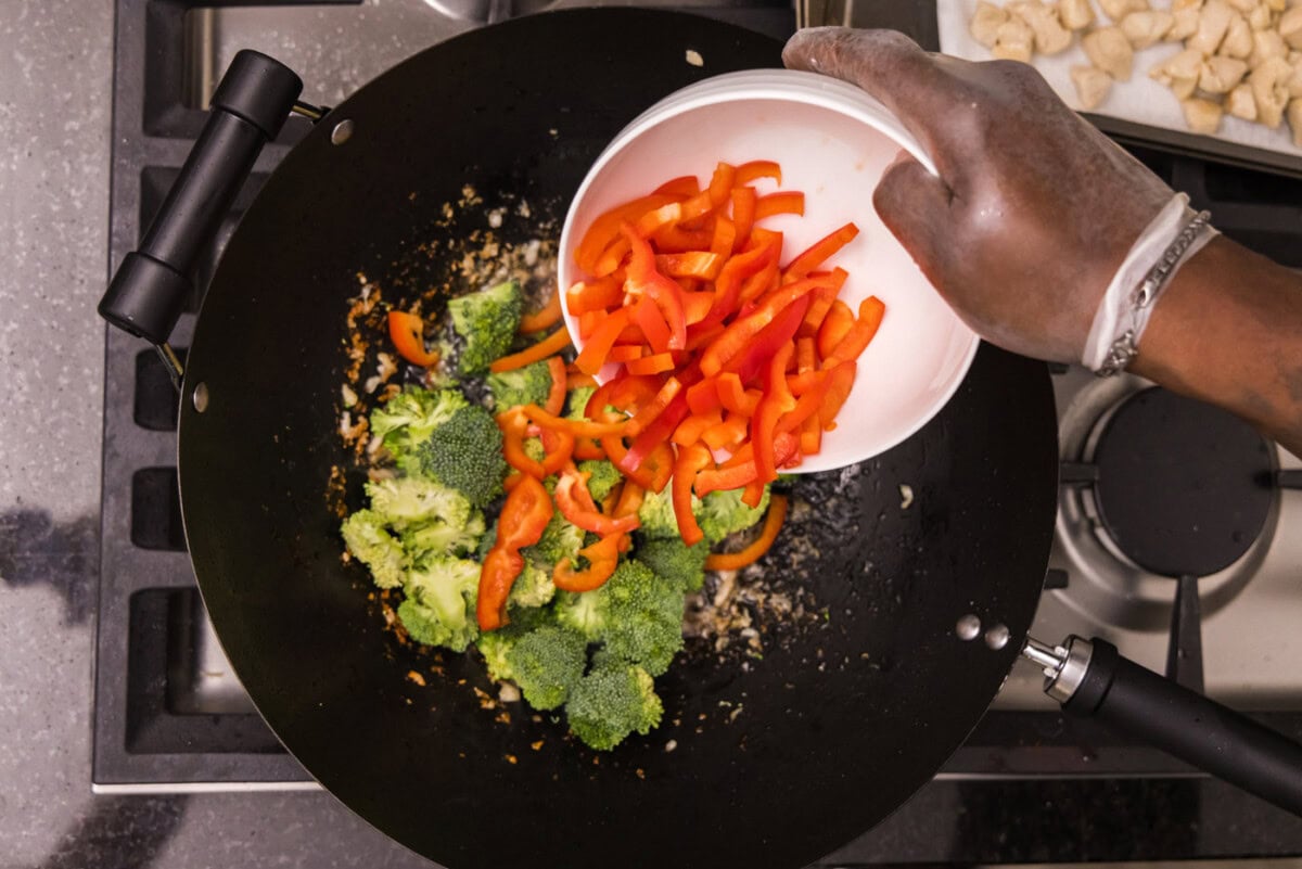 adding sliced red bell pepper to wok with broccoli