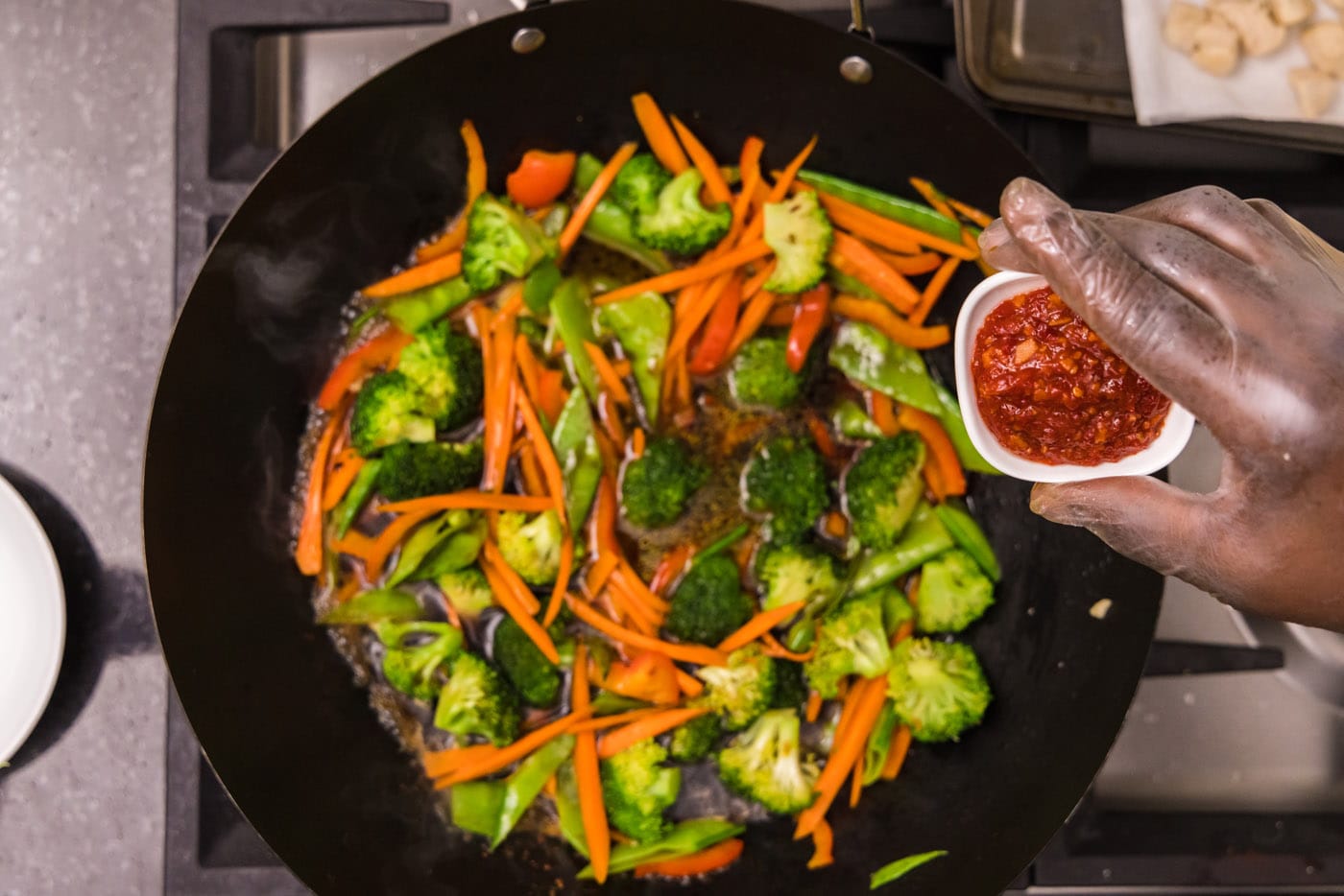 Asian chili garlic sauce over wok with vegetables