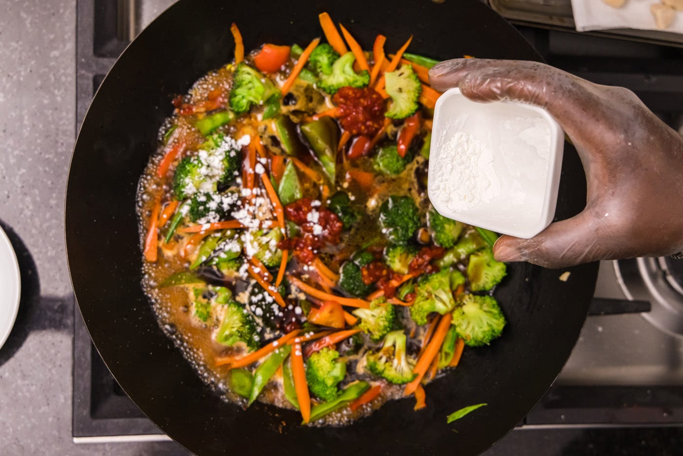 sprinkling cornstarch over veggies in a wok