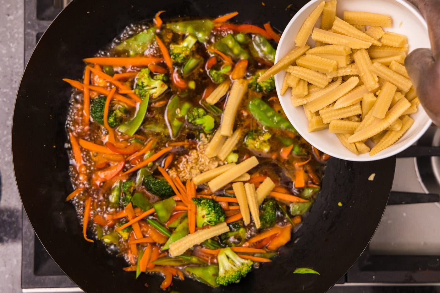 adding sliced baby corn to wok with vegetables