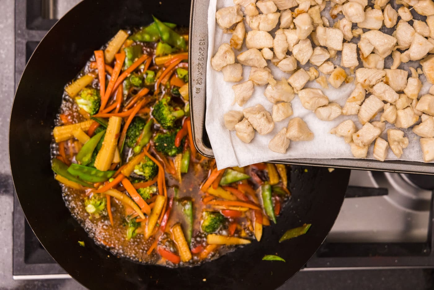 adding chicken back to wok with vegetables and sauce