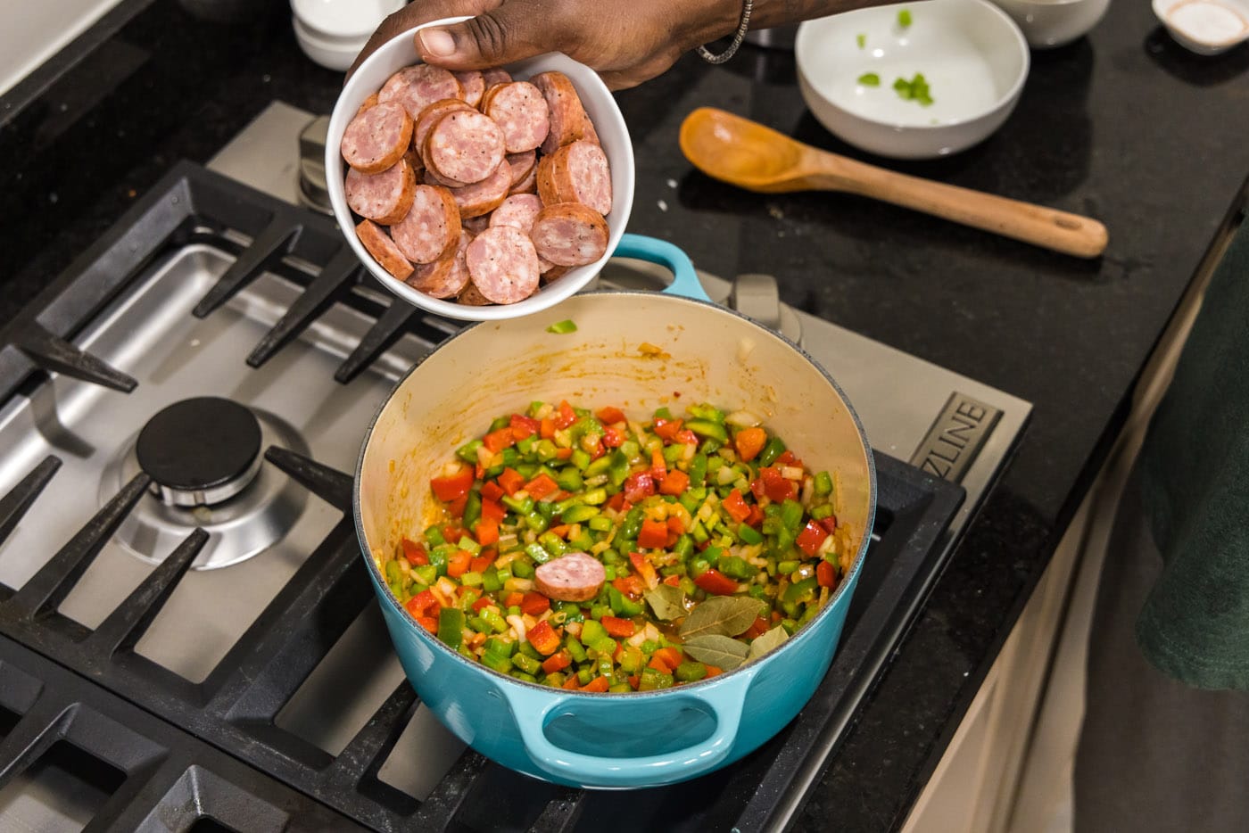 adding smoked sausage to pot with bell peppers, onion, and celery