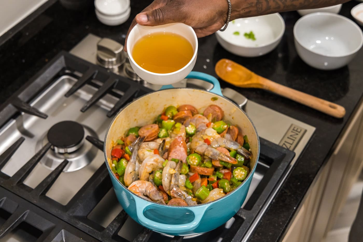 adding chicken broth to pot with shrimp, sausage, and vegetables