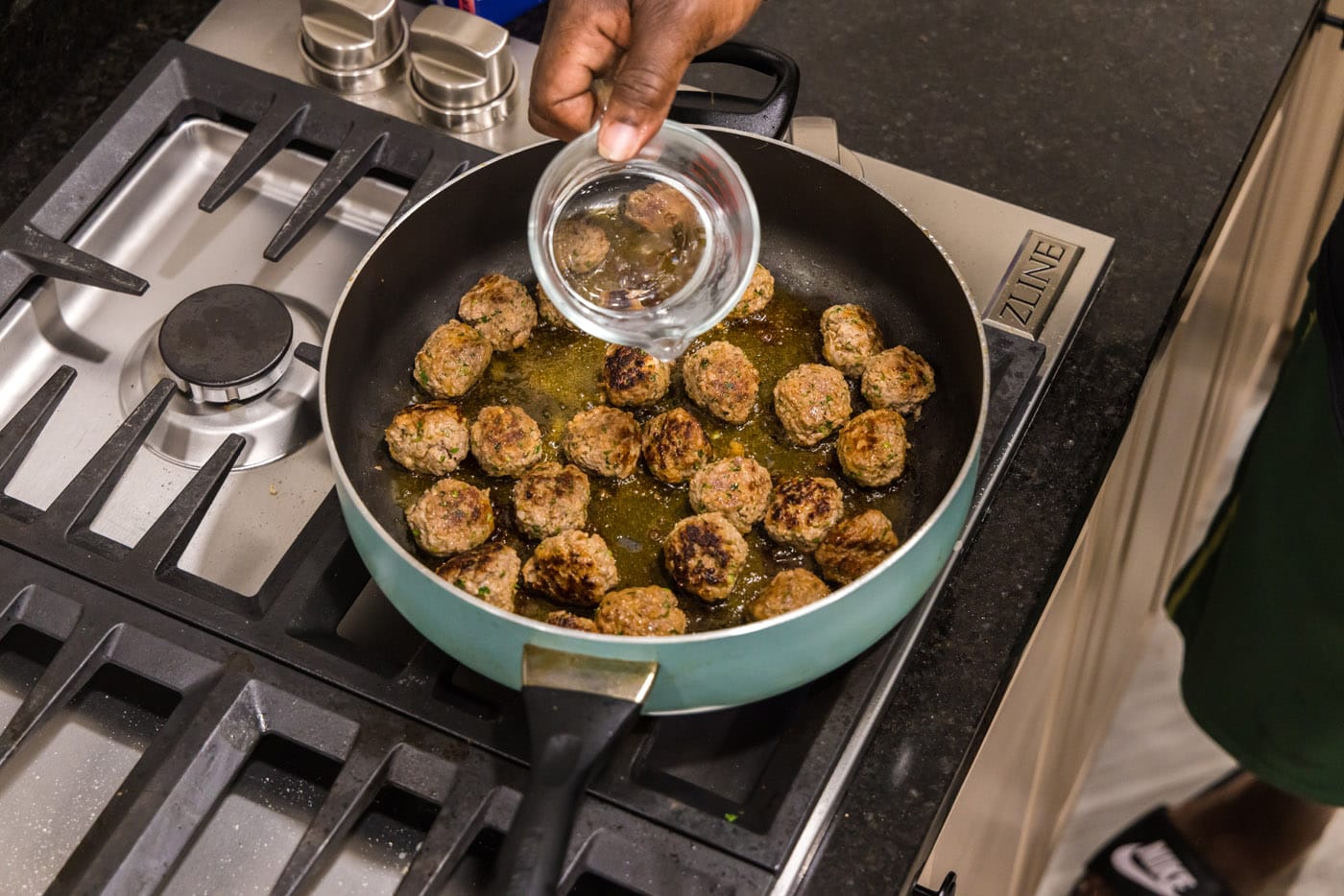 adding water to meatballs in a skillet
