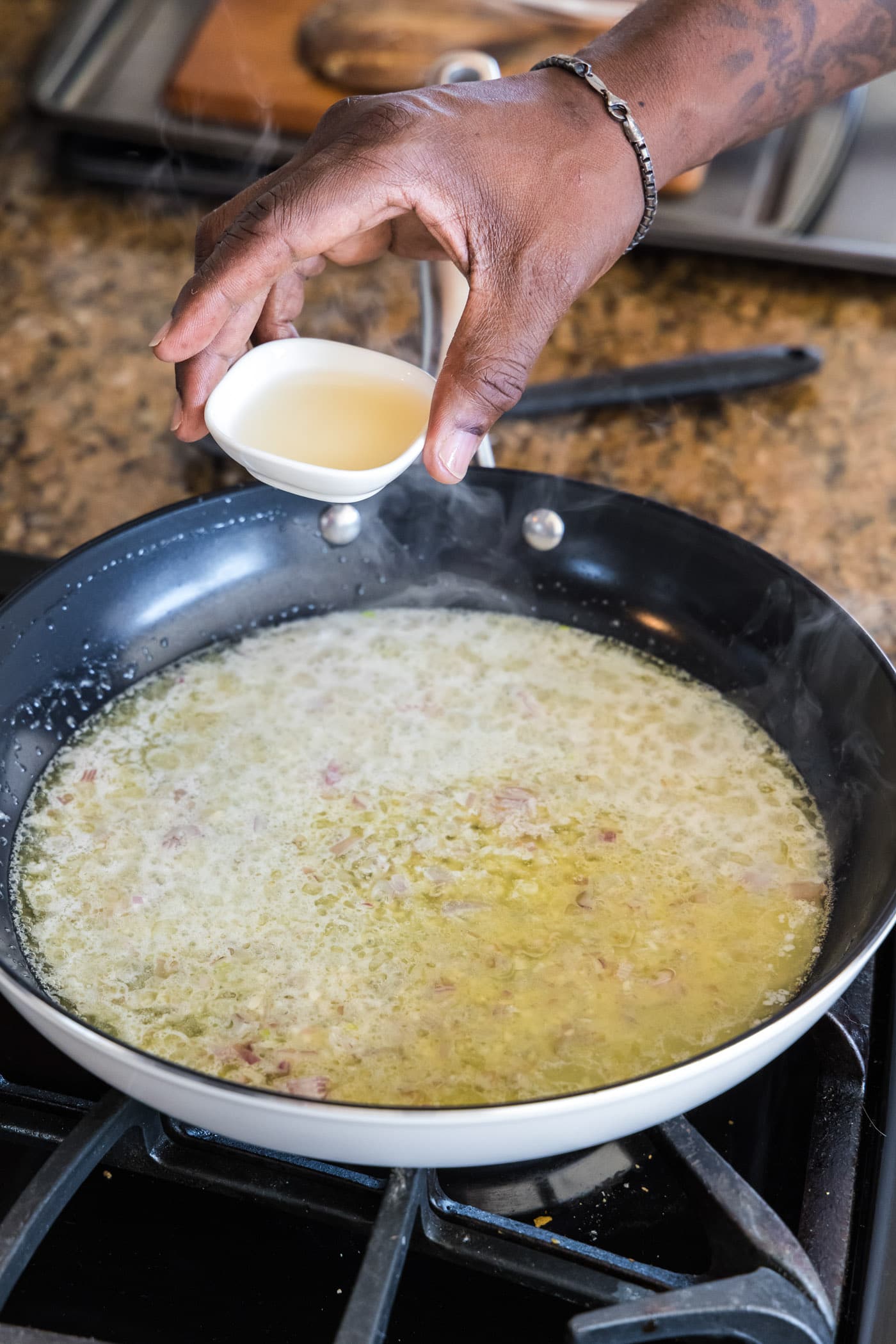 adding white wine to skillet of butter, shallots, garlic, and lemon juice