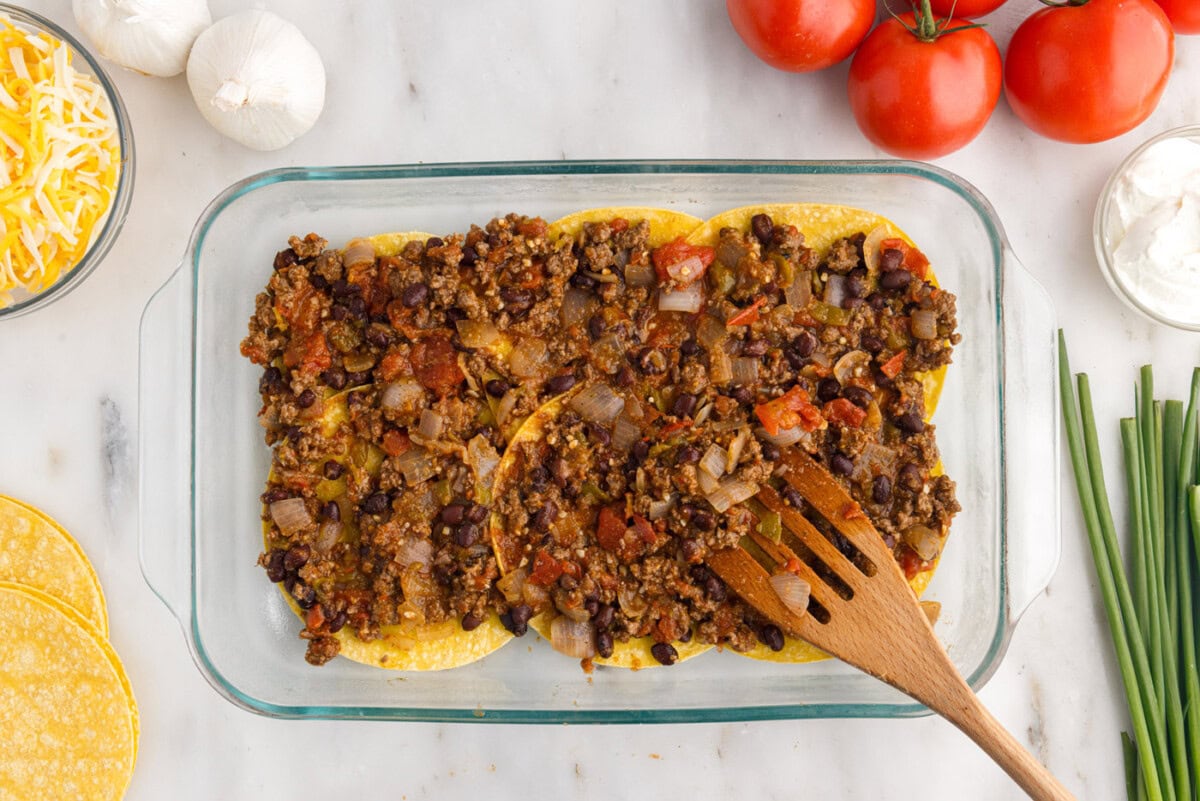 spreading meat mixture over corn tortillas