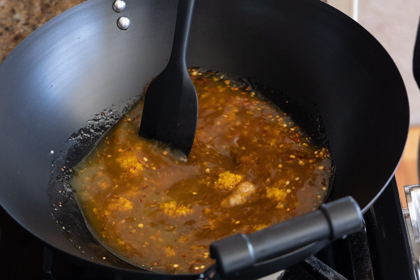 spatula stirring orange chicken sauce ingredients in a skillet