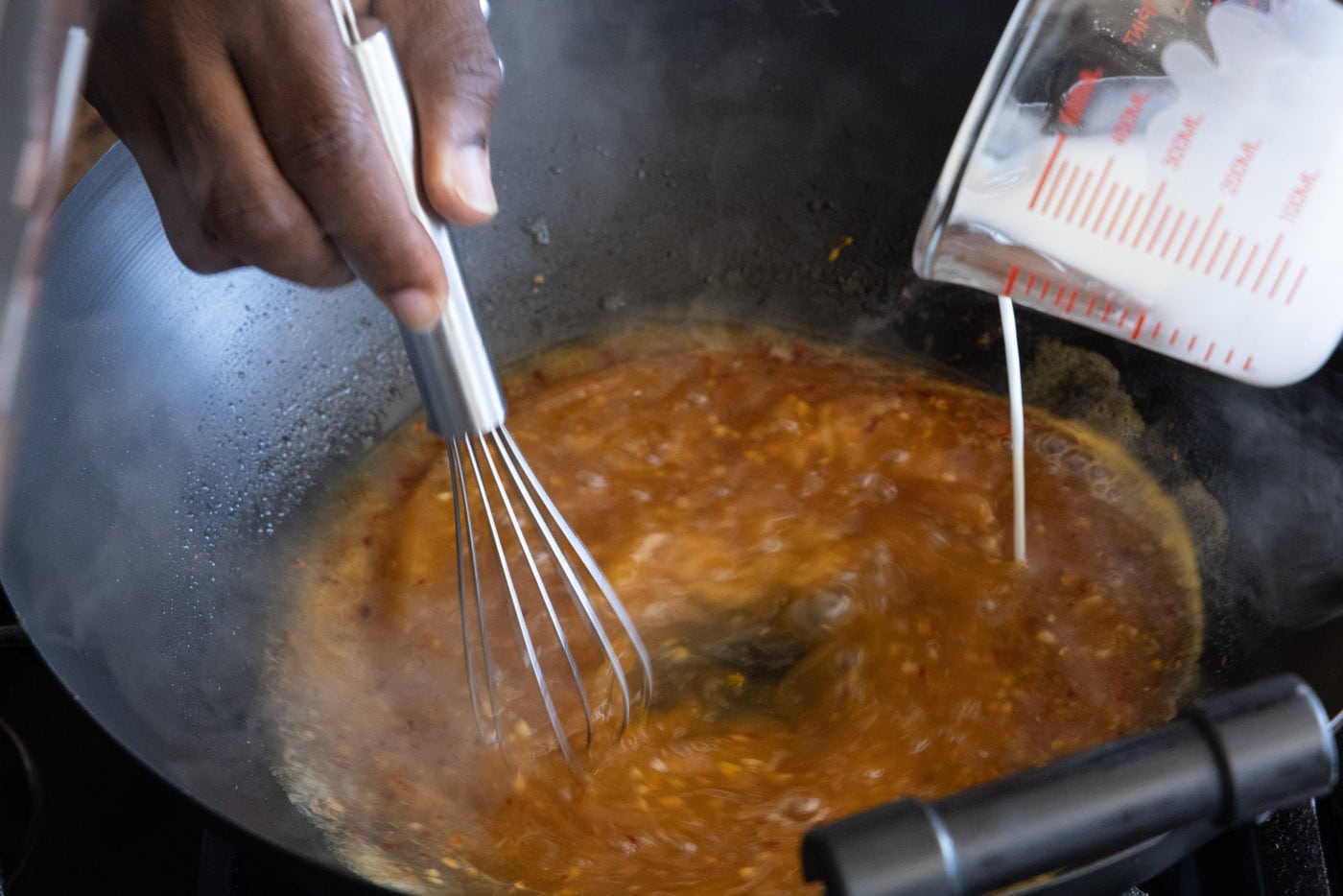 whisking cornstarch slurry into sauce in a skillet