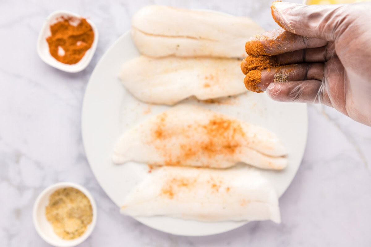 hand rubbing seasonings onto orange roughy filets