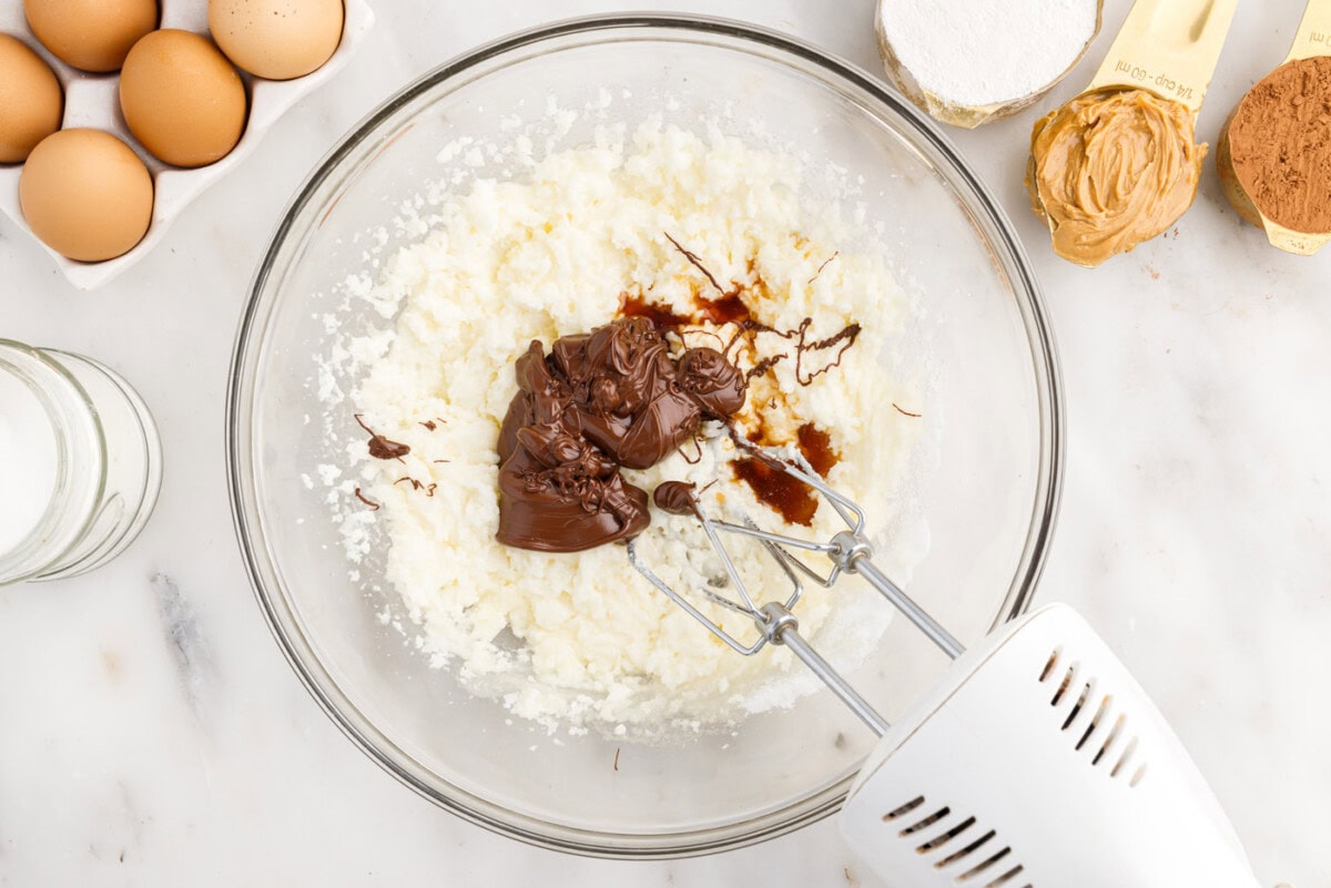 mixer combining melted chocolate and vanilla extract with butter and sugar mixture