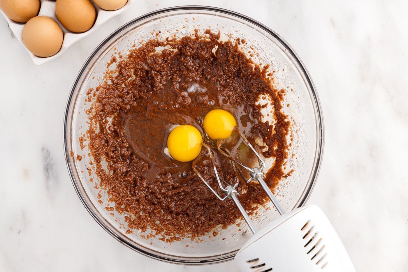 adding eggs to brownie batter in a mixing bowl