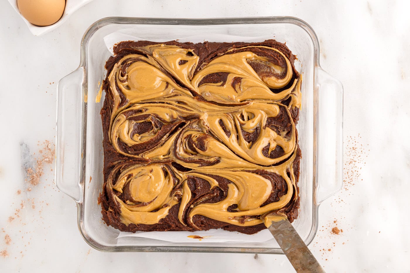butter knife swirling peanut butter on top of brownie batter in a pan